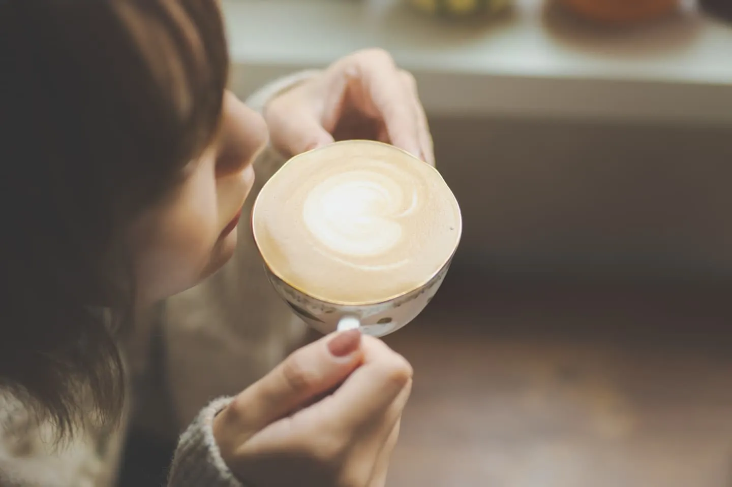 カフェラテのカップを持つ手元のイメージ写真